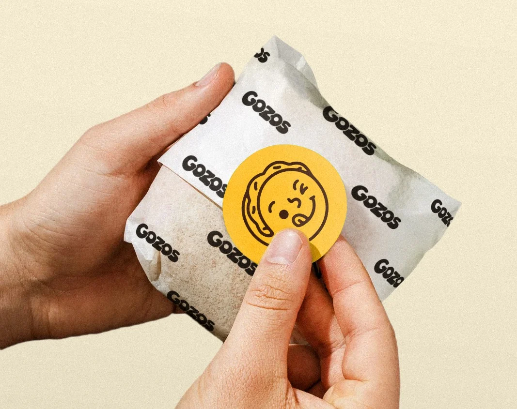 Hands pressing a Gozos sticker onto a wrapped arepa