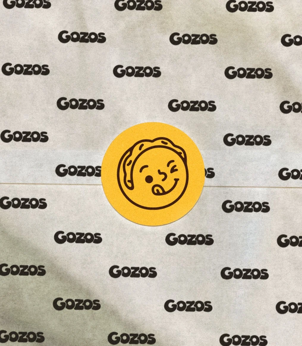 Gozos wrapping paper with the repeating wordmark, sealed with a mascot sticker