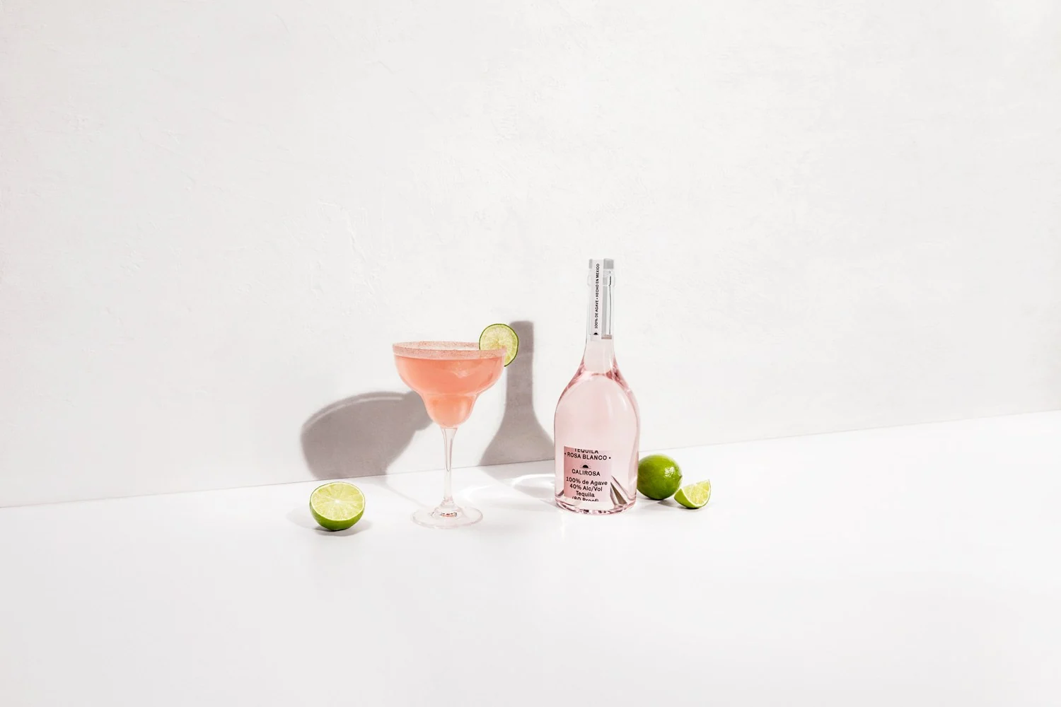 Rosa Blanco tequila bottle and cocktail with limes on white